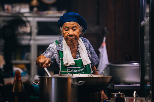 Bangkok, Thailand - January 12, 2024:
Close-up of a senior Thai woman preparing food outdoors at night.