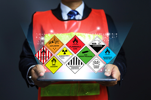 Hazardous substance concept chemical safety officer at dangerous goods warehouse holding tablet to arrange warning sign for different chemical to separate in sea transportation and air cargo shipment