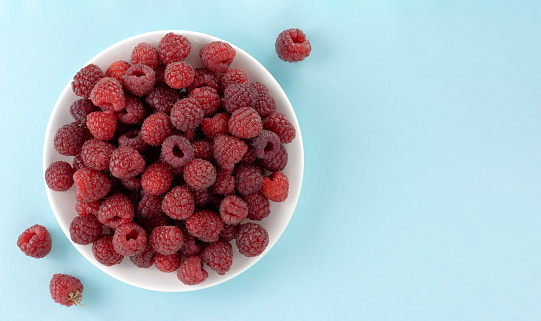 Fresh raspberries in a wooden bowl on a blue background. Top view.