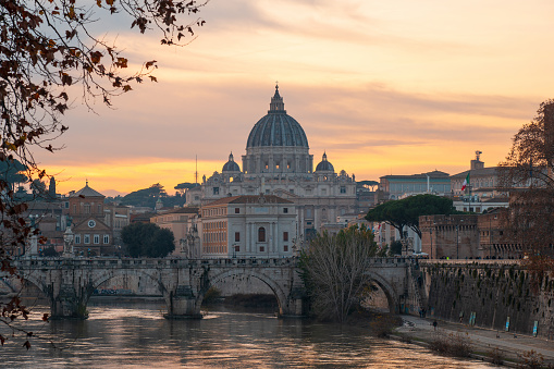 Rome, Italy - December 23,2022: St. Peter's Basilica in Rome, Italy, as the sun sets, casting a warm glow on the majestic structure, while the Tiber River gracefully reflects the colors of the Roman sky