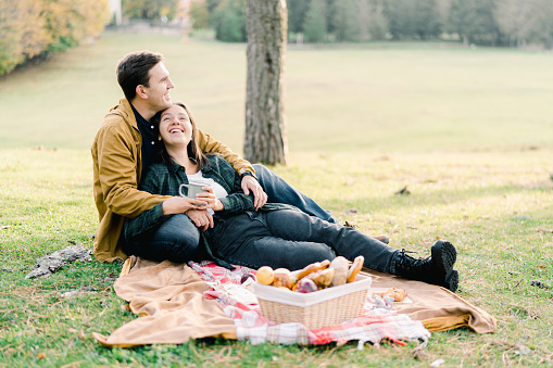 Smiling woman lying on blanket in park leaning against seated man. High quality photo