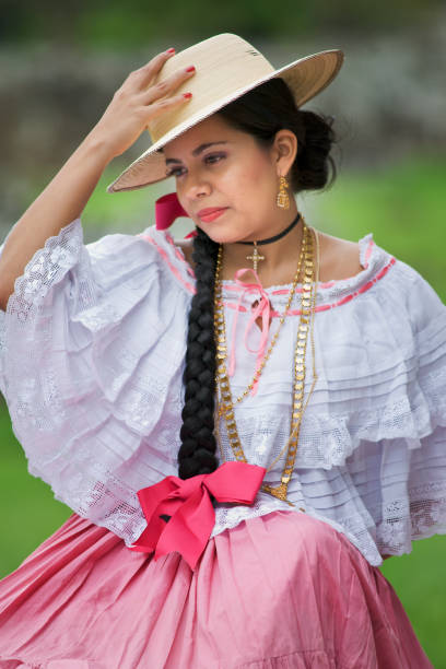 Pretty woman wearing a pink pollera and Panama hat, Panama's national costume, sits on ancient stones at the Panama la Vieja ruins,  Panama City, Panama, Central America