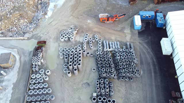Aerial view of an industrial site with stacks of concrete pipes and construction machinery.