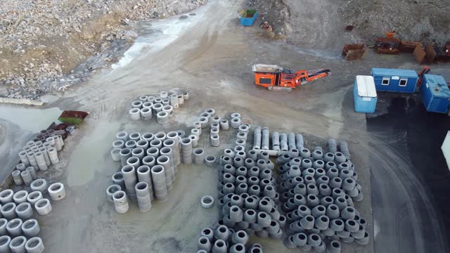 Aerial view of an industrial site with stacks of concrete pipes and construction machinery.