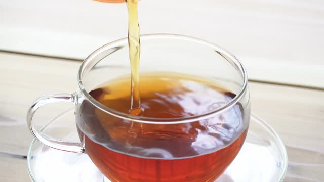 Pouring tea from a pot into a glass cup