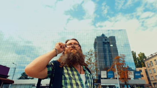 Elderly bearded man on a city background taking off his eyeglasses looking up