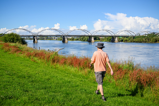 Man walking along Waikato river, Tainui Bridge in the background. Huntly. New Zealand.