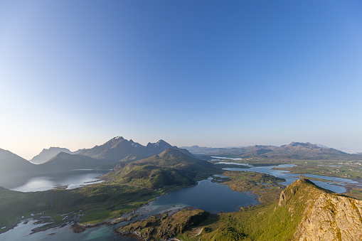 The midnight sun casts a tranquil haze over Offersoykammen, with the Nappstraumen's calm waters nestled among the verdant hills of Lofoten, Norway