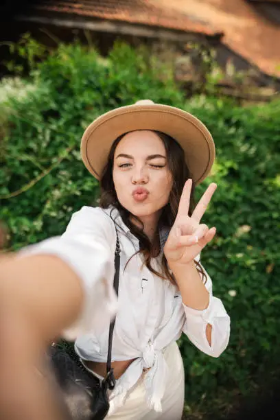 Portrait of young lady wear summer hat smiling showing v-sign taking selfie outdoors urban city park. Copy space
