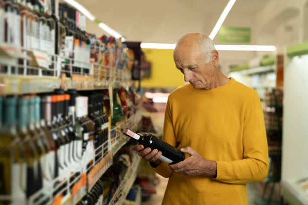 starszy mężczyzna wybiera wino w sklepie. starszy mężczyzna czyta etykietę na butelce wina przed zakupem - wine bottle liquor store wine variation zdjęcia i obrazy z banku zdjęć