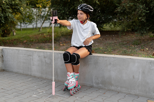 Teenage girl conducting a live broadcast explaining skating techniques in the park. Blogging and active leisure concept