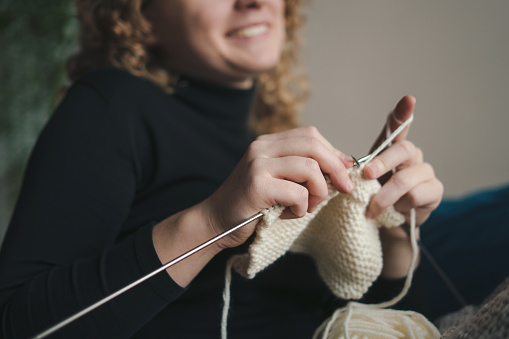 Close-up view of woman's hands knitting with knitting needles from yarn. Concept of cozy knitting at home. Cozy home and anti stress hobby.