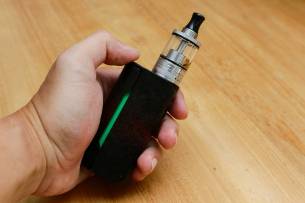 istock hand holding vape or e cigarette over wooden background 1947004249