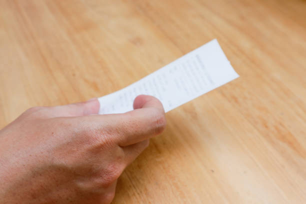 A man's hand is holding a shopping receipt on a wooden table