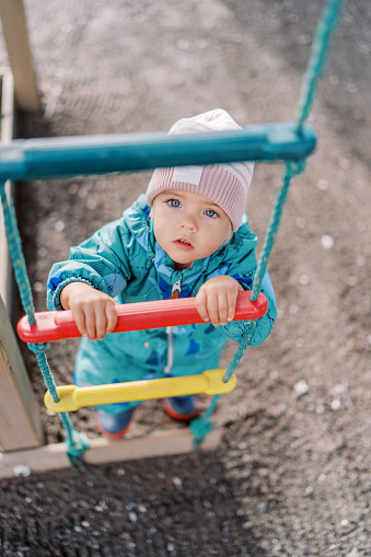 Little girl holds on to the rungs of a rope ladder and looks up. Top view. High quality photo