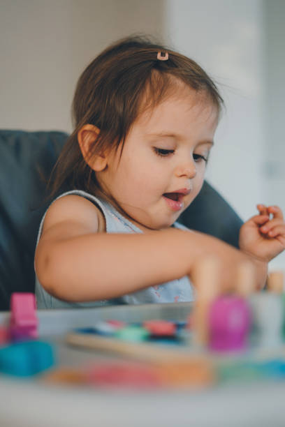 linda niña jugando con bloques de madera de colores en la silla del niño. desarrollo infantil temprano. - sorter fotografías e imágenes de stock