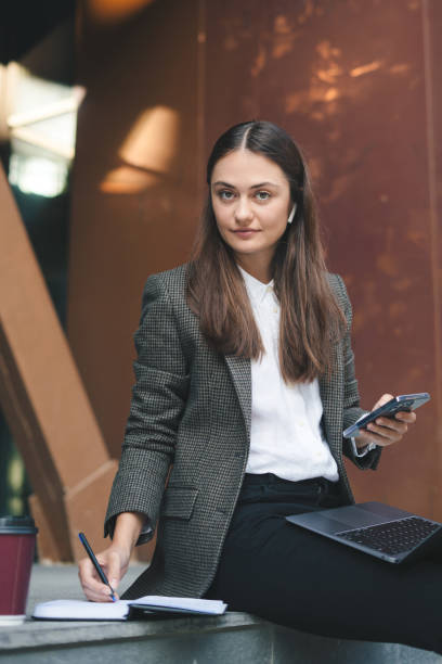 businesswoman sitting outdoors with laptop and making notes in her diary. freelancer female working while having a break. - surfing wireless vertical outdoors lifestyles imagens e fotografias de stock