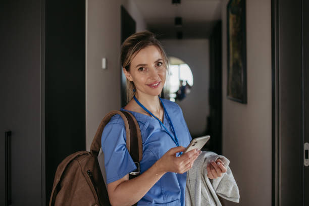 istock Female doctor getting ready for work, reading message on smartphone, leaving house in scrubs with backpack. Work-life balance for healthcare worker. 1947032068