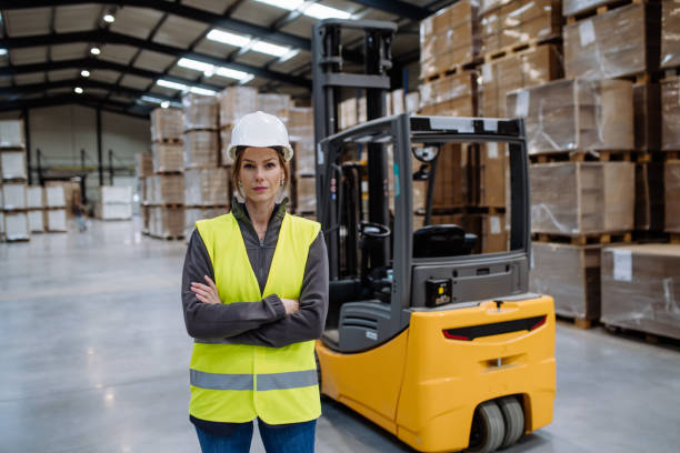 istock Female warehouse worker standing by forklift. Warehouse worker preparing products for shipmennt, delivery, checking stock in warehouse. 1947039456