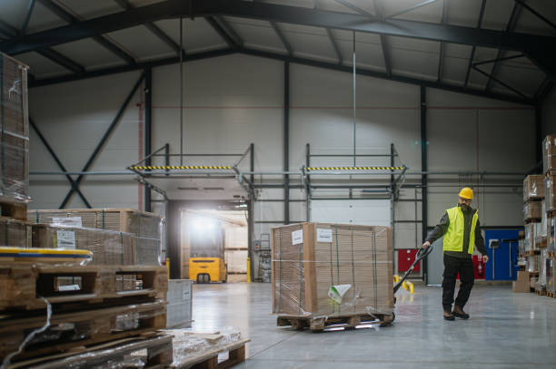 istock Warehouse worker maneuvering pallet jack loaded with goods through warehouse. 1947044753