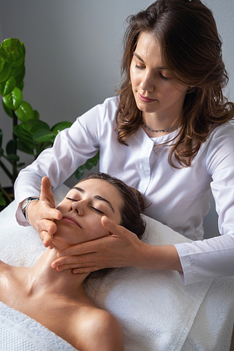 Young woman enjoying massage in spa salon, relaxed mature woman lying on table with closed eyes, getting anti-aging treatments at spa salon. Face treatment. Facial treatment.