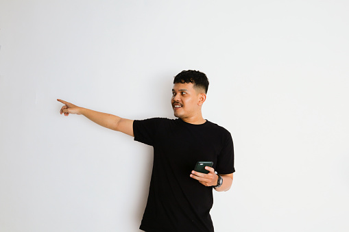 an Asian man points in a direction while holding his smartphone