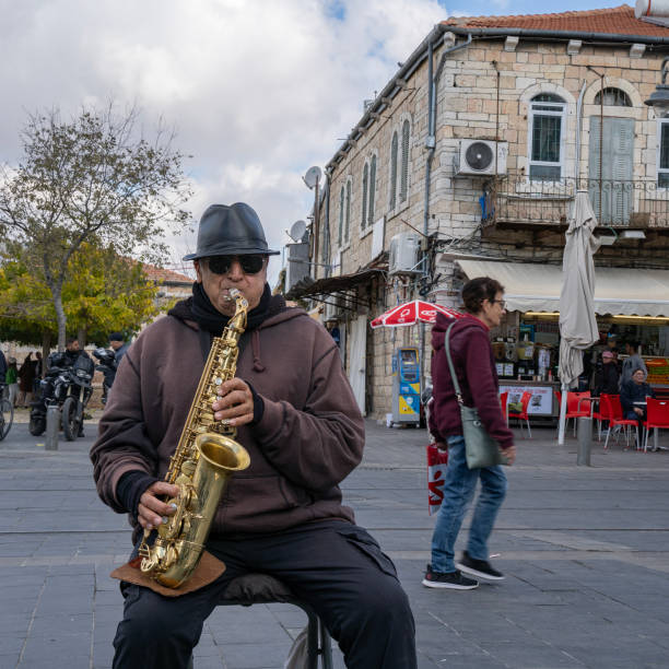 A focused saxophonist plays on a city street beside an intricately designed iron gate and stone architecture, capturing live music energy and urban culture.