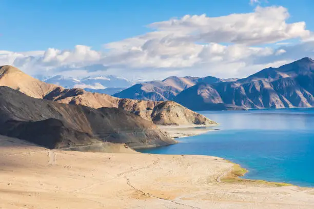 Pangong Tso or Pangong Lake is an endorheic lake spanning eastern Ladakh and West Tibet situated at an elevation of 4.225 m. It is 134 km long and divided into five sublakes, called Pangong Tso, Tso Nyak, Rum Tso (twin lakes) and Nyak Tso. Approximately 50% of the length of the overall lake lies within Tibet in China, 40% in Ladakh, India and the remaining 10% is disputed and is a de facto buffer zone between India and China. The lake is 5 km wide at its broadest point. All together it covers almost 700 km2.
Two streams feed the lake from the Indian side, forming marshes and wetlands at the edges. In the sun, the lake is a deep shimmering blue and green backed by barren tan-colored mountains with snows depending on the season, the sight that is stunningly beautiful and pristine. Despite being saline water the lake freezes completely during the winter. The spectacular lakeside is open during the tourist season, from May to September.
Pangong Tso, Ladakh, India, Asia.