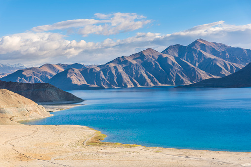 Pangong Tso or Pangong Lake is an endorheic lake spanning eastern Ladakh and West Tibet situated at an elevation of 4.225 m. It is 134 km long and divided into five sublakes, called Pangong Tso, Tso Nyak, Rum Tso (twin lakes) and Nyak Tso. Approximately 50% of the length of the overall lake lies within Tibet in China, 40% in Ladakh, India and the remaining 10% is disputed and is a de facto buffer zone between India and China. The lake is 5 km wide at its broadest point. All together it covers almost 700 km2.\nTwo streams feed the lake from the Indian side, forming marshes and wetlands at the edges. In the sun, the lake is a deep shimmering blue and green backed by barren tan-colored mountains with snows depending on the season, the sight that is stunningly beautiful and pristine. Despite being saline water the lake freezes completely during the winter. The spectacular lakeside is open during the tourist season, from May to September.\nPangong Tso, Ladakh, India, Asia.