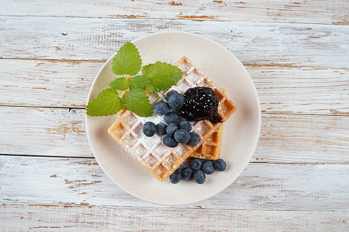 Delicious waffles with blueberry jam and fresh berries on wooden table