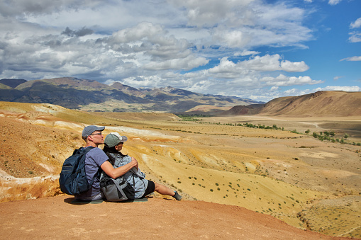 couple of tourists sit with their backs to camera against backdrop of landscape on summer day. Sights of Russia, Siberia and Altai Republic, mars. Tourism and travel. Kosh-agach, Chagan-Uzun