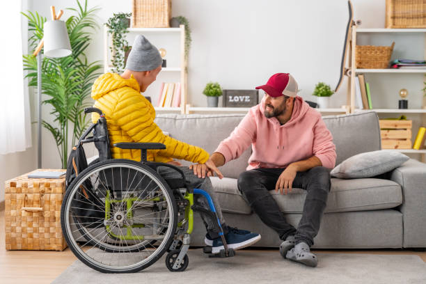 istock Man supporting a disabled friend in wheelchair at home 1947164077