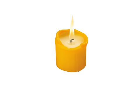 Yellow burning candle with bright flame isolated on white. Christmas holiday lights. Decorative colorful home illumination.\nTranslucent melting wax and black wick.