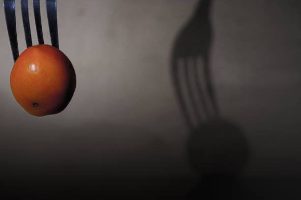 the shadow on the wall of a fork stabbing a fruit, cherry tomato