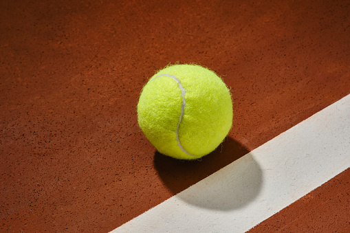 Tennis ball on a orange court surface with white stripe. Shallow depth of field