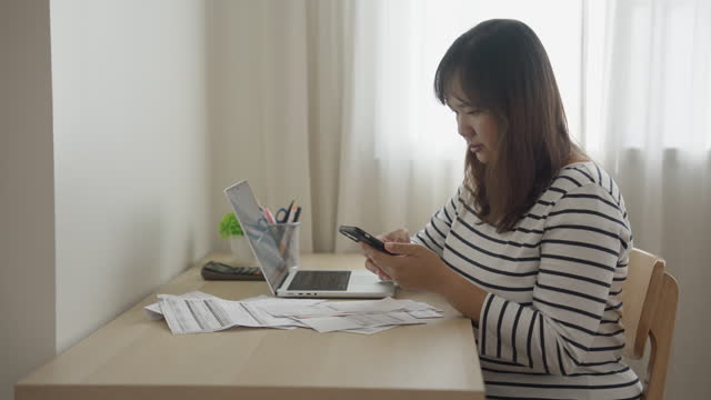 Asian woman managing and paying home financial bills online using a smart phone