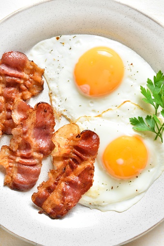 Close up view of fried eggs with bacon on plate. Top view, flat lay