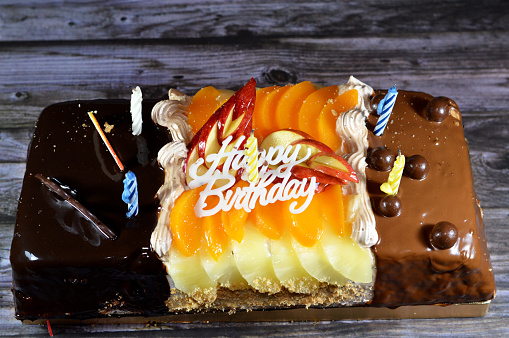 Birthday cake of three different pieces spongy creamy cake for celebrations, hazelnut chocolate spread, dark chocolate, caramel, whipped vanilla cream, slices of pineapples, apples, peach and nuts, selective focus