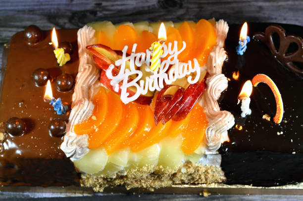 Birthday cake of three different pieces spongy creamy cake for celebrations, hazelnut chocolate spread, dark chocolate, caramel, whipped vanilla cream, slices of pineapples, apples, peach and nuts, selective focus