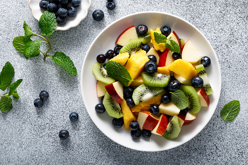Fruit and berry salad with mango, kiwi, apple, blueberry and fresh mint leaves. Healthy food, diet. Top view
