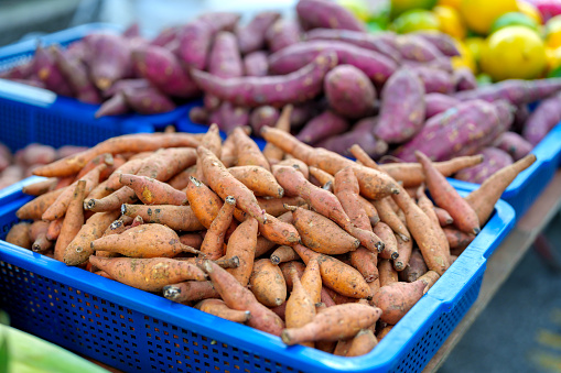 In a close-up view, a pile of sweet potatoes is showcased at an Asian morning market stall, inviting customers with their vibrant colors and fresh appeal.