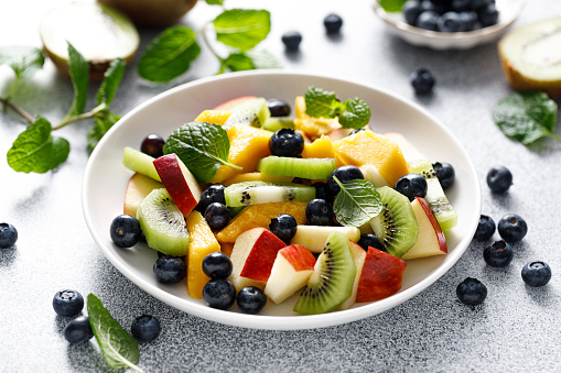 Fruit and berry salad with mango, kiwi, apple, blueberry and fresh mint leaves. Healthy food, diet