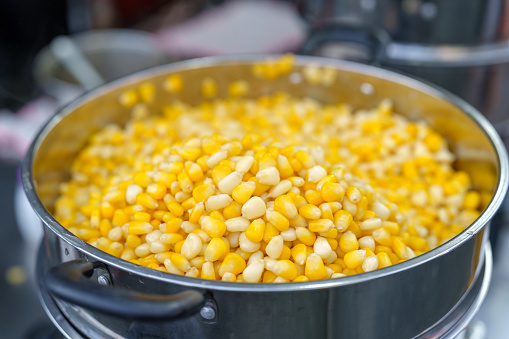 A close-up shot of steamed corn on a metal steamer tray, preparing food for sale at an Asian night market.