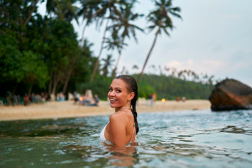 Happy swimmer in tropical ocean. Lady with long-lasting makeup in sea. Stylish bikini on travel. Delighted tourist submerged in water. Female experiencing coastal vacation atmosphere.
