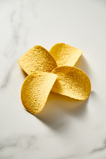 Four potato chips flower-shaped on white marble background. Minimalistic food photo. High quality photo