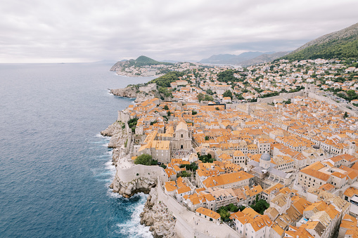 Red roofs of ancient houses behind high fortress walls on the seashore. Dubrovnik, Croatia. Drone