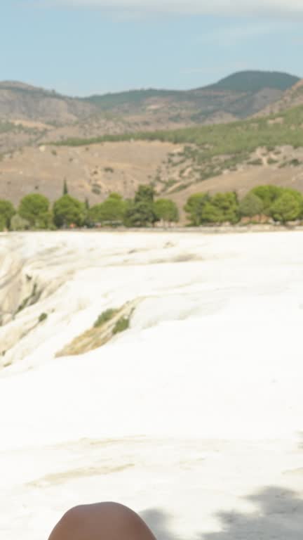 Vertical video. At the top of the White Mountain formed from calcium, a young woman sits on a bridge, enjoying the high-altitude view. Exploring incredible places on Earth.