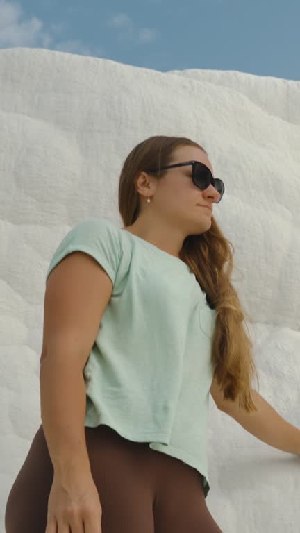 Vertical video. A young woman stands at the edge of a natural pool with a backdrop of white travertine rock. A unique location in Pamukkale.