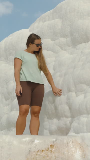 Vertical video. A pristine white rock, a natural formation of travertine. A woman touches and examines it while standing in a natural pool.