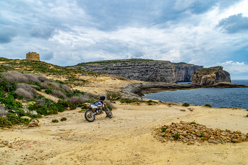 Dwejra, Gozo - April 3rd 2019: A motorbike on the shore in Dwejra. In the background is the Dwejra Tower and the islet Fungus Rock aka Il-ebla tal-eneral (The General's Rock).